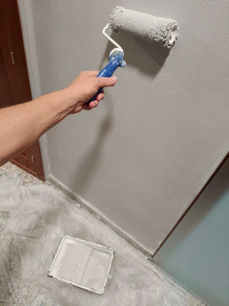 Aplicación con rodillo de pintura gris en una pared reparada
